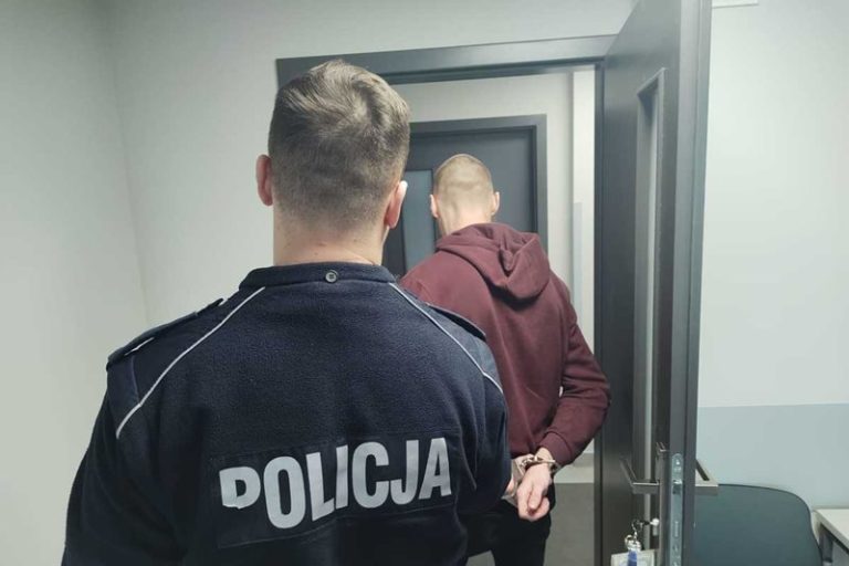 Policjant prowadzi zatrzymanego podejrzanego o usiłowanie zabójstwa
