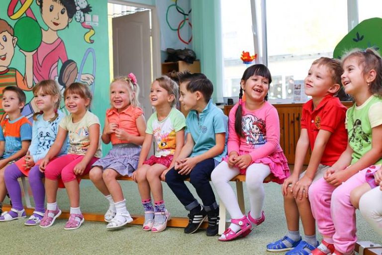 dzieci w przedszkolu siedzące na ławeczce