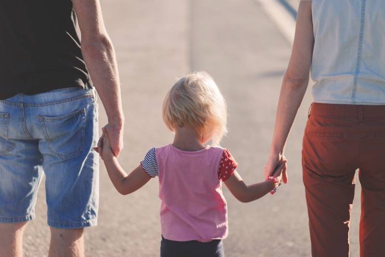 rodzina zastępcza; matka z ojcem trzymają dziecko za rękę, widok od tyłu
