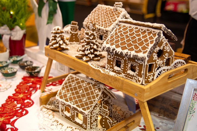 Na świątecznym stole położony jest domek zrobiony z piernika z białym lukrem, obok domku znajdują się bałwanki oraz choinki z piernika