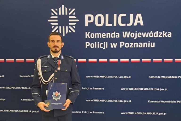 Komisarz Łukasz Wodziński z Turku na tle ścianki z logotypem Komendy Wojewódzkiej Policji w Poznaniu