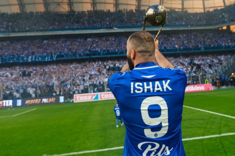 Mikael Ishak prezentuje puchar za mistrzostwo Polski w 2025 r. Ishak od tyłu, zwrócony w kierunku trybun podnosi do góry puchar