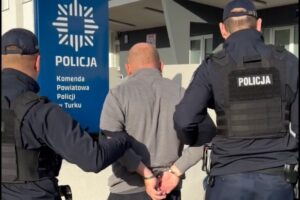 Turek. Policjanci prowadzą zatrzymanego nietrzeźwego kierowcę, skutego kajdankami.